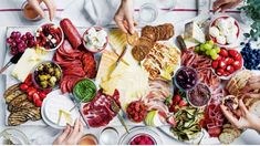 several people are serving food on a platter with cheeses, meats and fruit