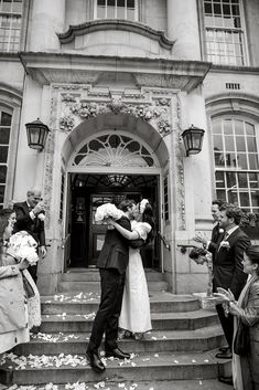 a bride and groom kiss on the steps of an old building as their guests look on