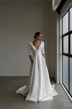 a woman in a white wedding dress standing by a window with her back to the camera