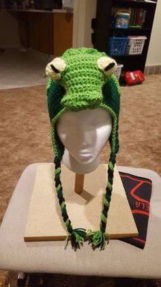 a crocheted frog hat sitting on top of a mannequin's head