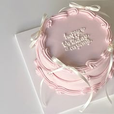 a pink birthday cake sitting on top of a white plate with a ribbon around it