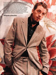 a man wearing a suit and tie standing in front of a flowered wall with his hands in his pockets