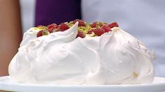 a cake with white frosting and raspberries on top sitting on a plate