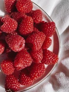 a glass bowl filled with raspberries on top of a white cloth