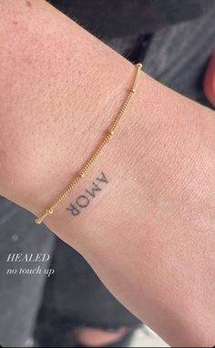 a woman's arm with the word bow on it and a gold chain bracelet