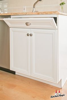 a white kitchen with an island sink and wooden flooring in front of the cabinets