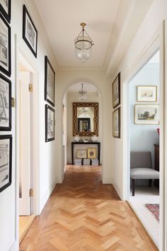 a hallway with pictures on the wall and wood flooring, along with a chandelier