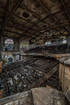 an old abandoned building with lots of wooden chairs in the center and many windows above it