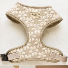 the dog harness is beige with white flowers on it's front and back side