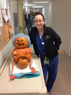 a woman in scrubs standing next to a carved pumpkin