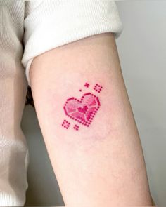 a small pink heart tattoo on the left inner arm, with squares and dots all over it