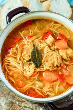 a bowl of chicken noodle soup with bread in the background