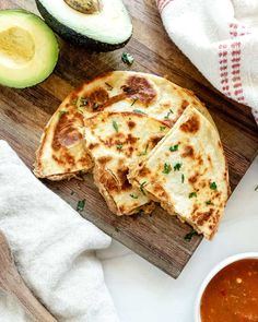 two quesadillas on a cutting board with salsa and avocado