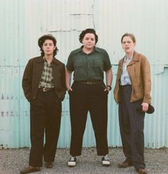 three women standing next to each other in front of a metal building with a blue wall behind them