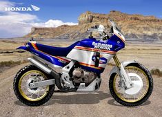 a blue and white motorcycle parked on top of a dirt road in the middle of nowhere