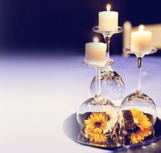 two wine glasses with sunflowers in them are sitting on a table next to candles