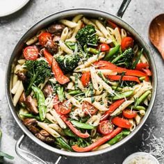 a pan filled with pasta and vegetables on top of a table next to utensils