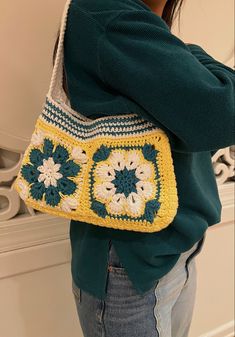 a woman is holding a crocheted bag with flowers on the front and sides