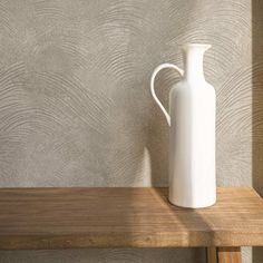 a white vase sitting on top of a wooden shelf next to a wallpapered wall