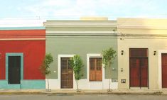 two buildings with red doors and green trees on the side of the street in front of them