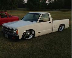 a white pick up truck parked next to a red pickup truck in a grassy field