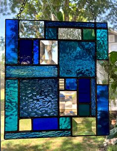 a stained glass window hanging from a chain in front of a tree and some grass