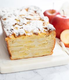 a piece of cake sitting on top of a white cutting board next to an apple