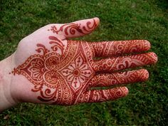 a person's hand with red henna on it and green grass in the background