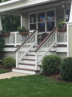 a white house with stairs leading up to the front door and flowers in pots on the porch