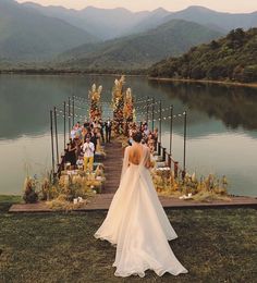 a woman in a wedding dress is standing on a dock near the water with people