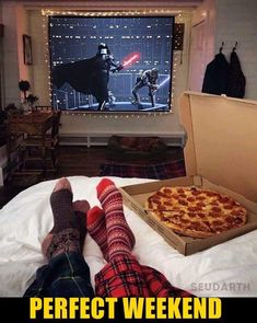 two people laying on a bed in front of a tv with a large pizza in it