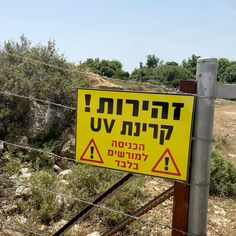 a yellow sign that is on the side of a fence in front of some bushes