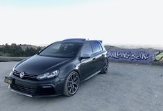 a black car parked in front of a graffiti covered wall