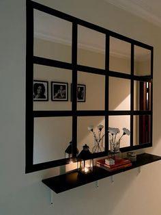 a mirror is hanging on the wall above a shelf with candles and flowers in it