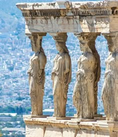 some statues on the side of a building with a city in the backgroud