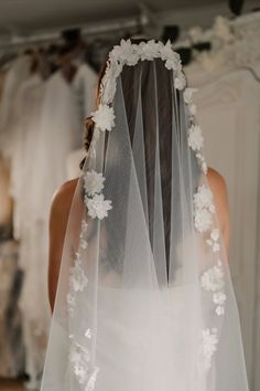 the back of a bride's veil with white flowers on it, in front of her wedding dress