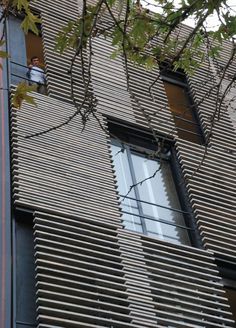 a man is standing on the window sill in front of an apartment building with vertical blinds