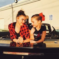 two young women sitting next to each other in front of a car with the caption's name on it