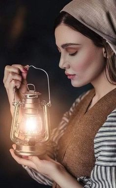 a woman is holding a lantern in her hands and looking down at the light on it