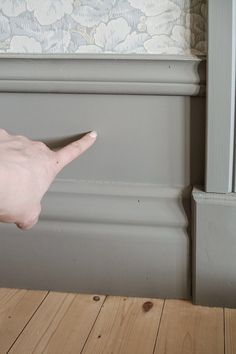 a person's hand reaching for the corner of a wall in front of a window