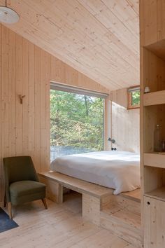 a bedroom with wooden walls and flooring has a bed, bookcases, and chair