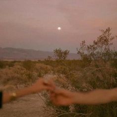 two people reaching out their hands to touch each other in the desert at night time