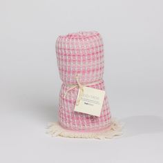 a pink and white plaid blanket with a tag on the end, sitting in front of a gray background