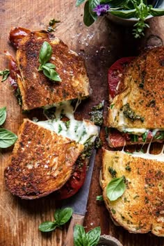 four slices of pizza on a wooden cutting board with basil and tomatoes in the background