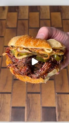 a hand holding a sandwich on top of a wooden table next to a tiled floor