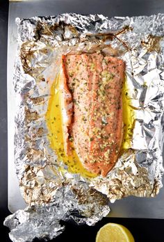 a piece of salmon on tin foil with lemon wedges and seasoning next to it