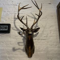 a deer head mounted to the side of a white brick wall next to a sign