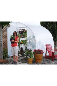 a woman standing in front of a small greenhouse