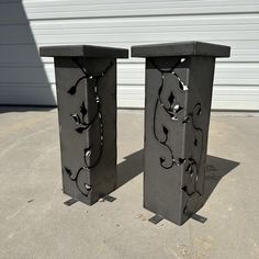 two black metal vases sitting on top of cement floor next to a garage door