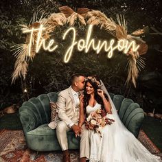 a bride and groom sitting on a couch in front of a neon sign that reads the johnson